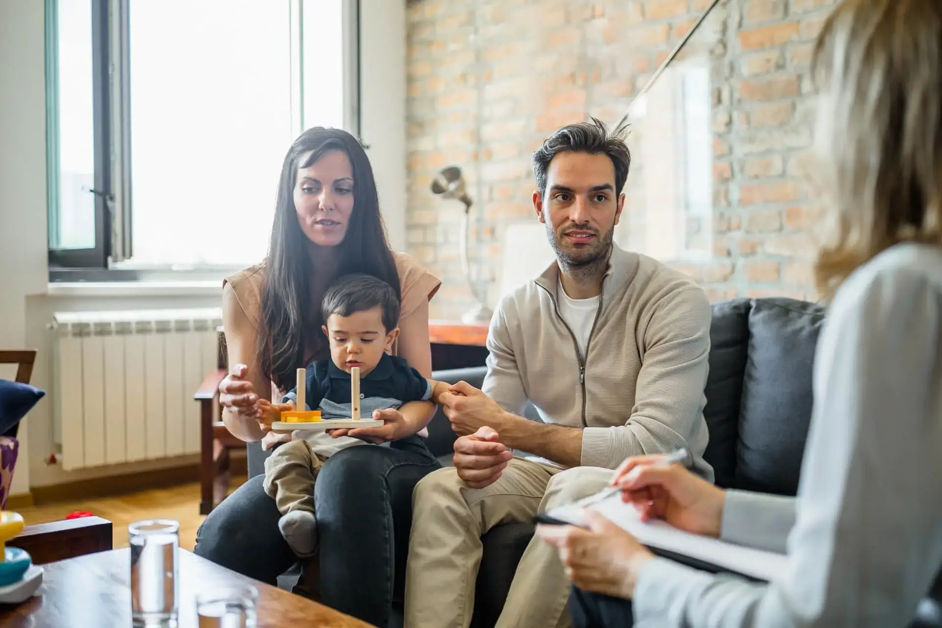 Kanepede küçük çocuklarıyla oturan bir aile ve karşılarında not alan bir uzman